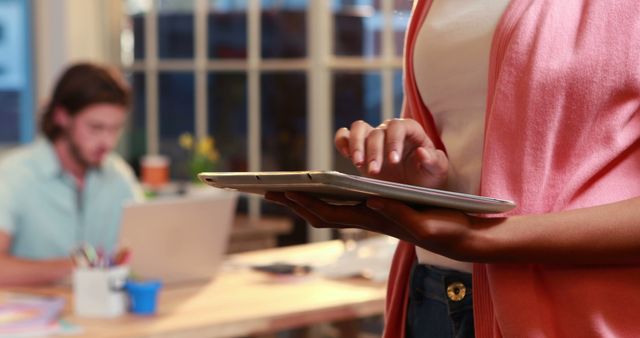 Woman Using Tablet While Colleague Works on Laptop in Office - Download Free Stock Images Pikwizard.com