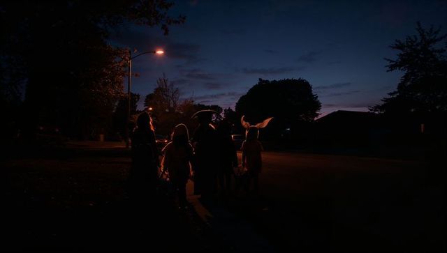 Children trick-or-treating at dusk in neighborhood with candy buckets
