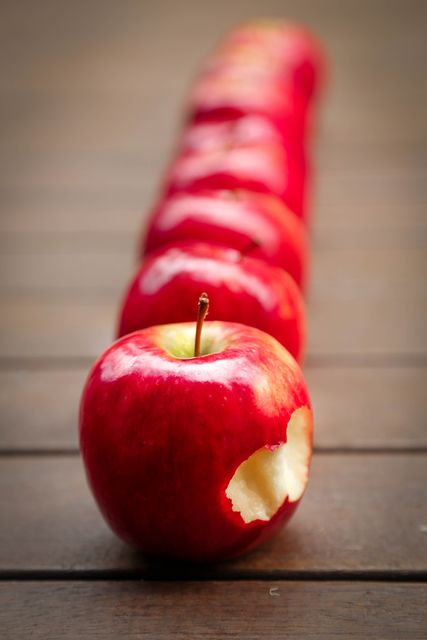 Quality image showing red apples arranged in a row, each having a single bite mark. Great for illustrating concepts of food, healthy eating, freshness, or first taste. Useful in marketing campaigns for food products, blogs on nutrition, and educational materials about fruits.