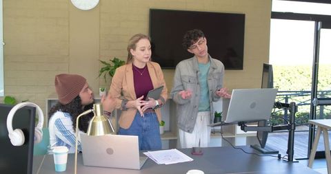 Young team presenting project using tablet and laptop in modern office with balcony view