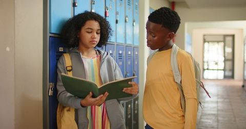 African american students checking binder and discussing notes by school lockers