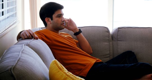 Man in Orange Shirt Relaxing on Couch and Talking on Phone - Download Free Stock Images Pikwizard.com