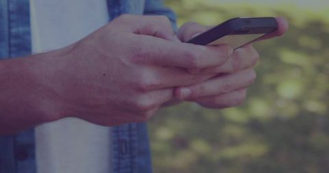 Closeup Hands Typing on Smartphone in Park Wearing Denim Shirt with Bokeh Greenery