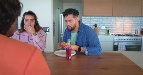Friends reacting and eating sandwich at kitchen island with pink beverage