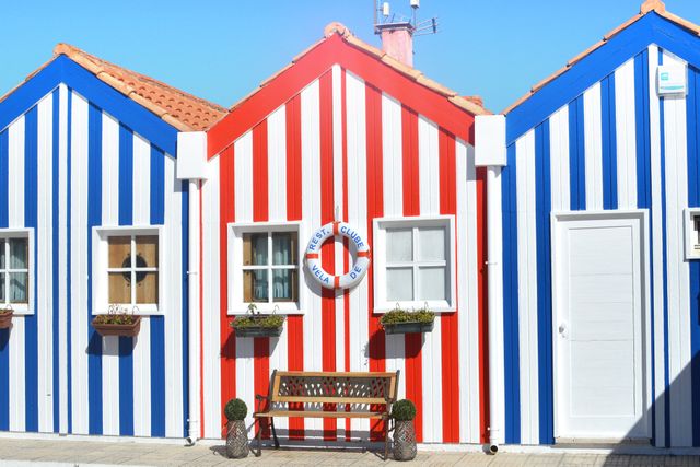 Vibrant striped beach houses in red and blue with a clear sky. Ideal for promoting travel destinations, vacation spots, or coastal lifestyle. Useful for summer-themed graphics, travel blogs, or postcards conveying a cheerful, sunny atmosphere.