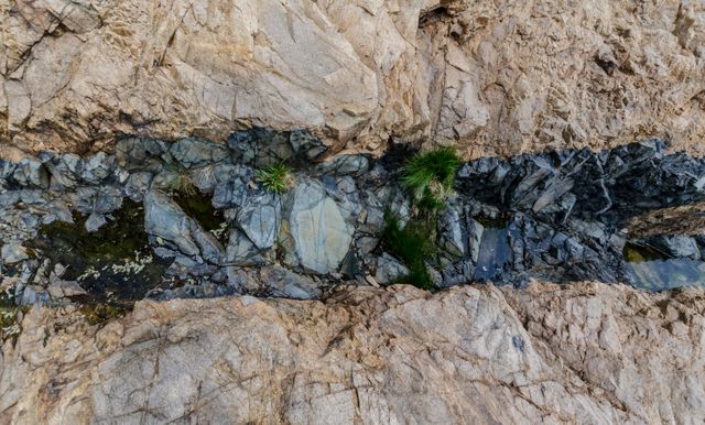Captured from above, this shows a narrow water stream running through rugged rocks with patches of green vegetation. Perfect for nature enthusiasts, geological studies, environmental projects, and educational materials focusing on natural geology and ecology.