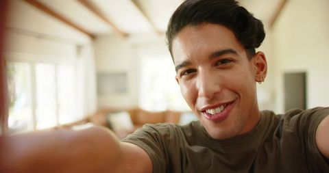 Smiling african american man taking selfie on cozy living room sofa with natural light