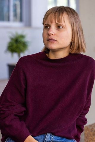 Pensive young woman wearing burgundy sweater and jeans gazing out window in modern room