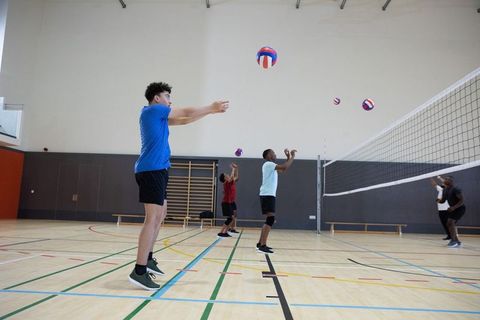 Young men practicing volleyball jumping, passing and serving in indoor gymnasium