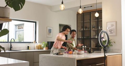 Diverse couple cooking together at modern kitchen island filming social media cooking content