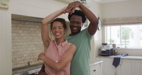 Joyful biracial couple dancing in kitchen together