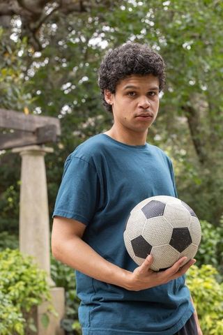 African man standing in green park holding soccer ball for sports lifestyle portrait