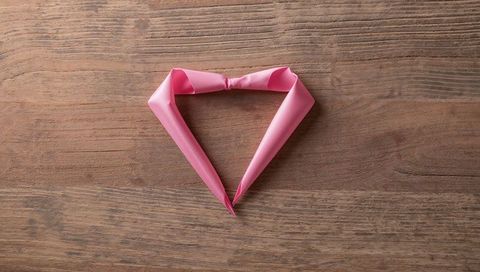 Heart-shaped pink satin ribbon on wooden tabletop