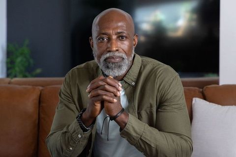 Senior african man reflecting on sofa with hands clasped, calm mature portrait