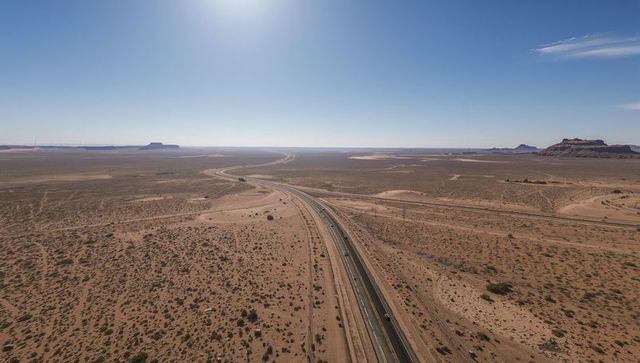 Curving Highway Stretching Across Vast Desert Plain Toward Distant Mesas Under Clear Sky