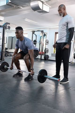 African American man deadlifting under guidance of senior trainer in modern gym session