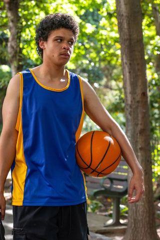 African american teen athlete standing in sunlit park holding orange basketball at hip