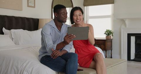 Couple using tablet for wedding planning in cozy bedroom