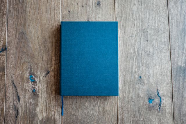 Blue hardcover book laying on a rustic wooden table. Perfect for themes on reading, education, journaling, creativity, literature, and interior decor. Ideal for websites, blogs, and articles on book-related topics and home aesthetics.