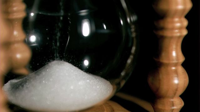 Hourglass sand falling in super slow motion symbolizes passing time. Perfect for concepts of time, deadlines, and patience metaphors in presentations or motivational content. Use in educational materials or decorative pieces related to time management and punctuality.