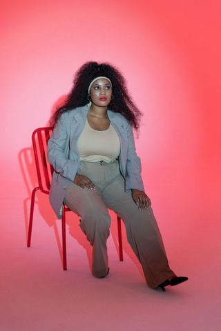 Confident african american woman sitting on red chair in studio wearing gray blazer