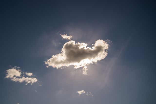 Image of a solitary cloud with sunlight streaming from behind, set against a clear blue sky. Ideal for concepts related to weather, nature, and tranquility. Suitable for background images, nature blogs, relaxation themes, and inspirational or motivational visuals.