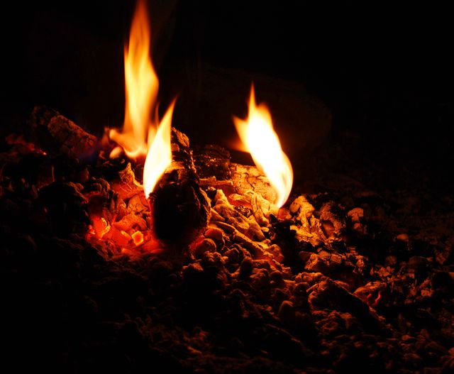 Warm glowing embers of a campfire in the dark create a cozy and relaxing atmosphere. This image can be used for topics related to camping, outdoor activities, warmth, and relaxation. Ideal for websites, blogs, or social media posts about outdoor adventures, campfire stories, or night settings.