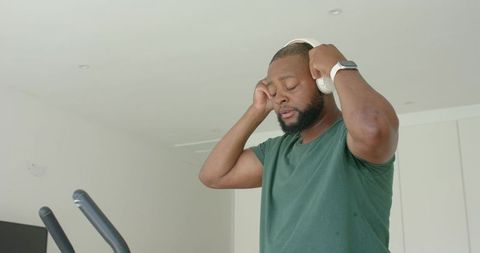 African man putting on headphones preparing for workout in modern bright home gym