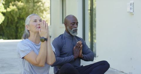 Diverse mature couple practicing outdoor meditation on patio for wellness