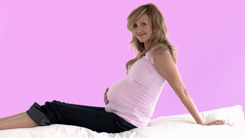 Pregnant Woman Relaxing on White Bedding Against Pink Background