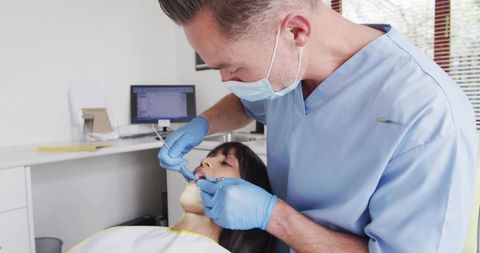 Dentist examining patient for dental checkup in modern clinic wearing mask and gloves