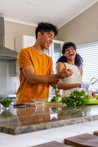 Couple laughing and cooking at kitchen island chopping herbs and squeezing lime