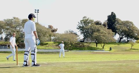 Cricket players batting on grass pitch during outdoor match