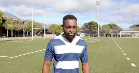 Focused Athlete Standing on Synthetic Turf Wearing Navy-Striped Jersey in Stadium