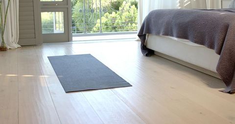 Sunlit Minimalist Bedroom Featuring Dark Gray Yoga Mat on Pale Hardwood Near Open Balcony