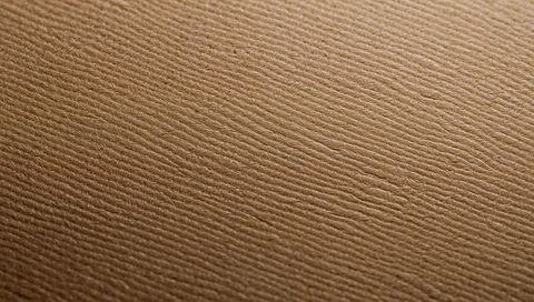 Kraft paper texture closeup showing diagonal ridges and warm soft lighting