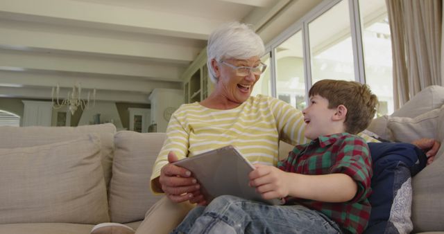 Elderly woman and young boy spending quality time, enjoying digital content indoors. Ideal for depicting family bonding, intergenerational relationships, and use of technology by seniors. Great for campaigns about senior technology use, family togetherness, or digital learning.