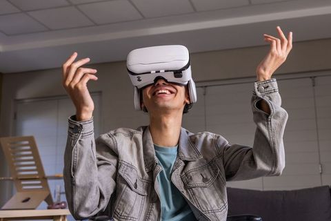 Teen male wearing white VR headset smiling and gesturing in cozy living room at home