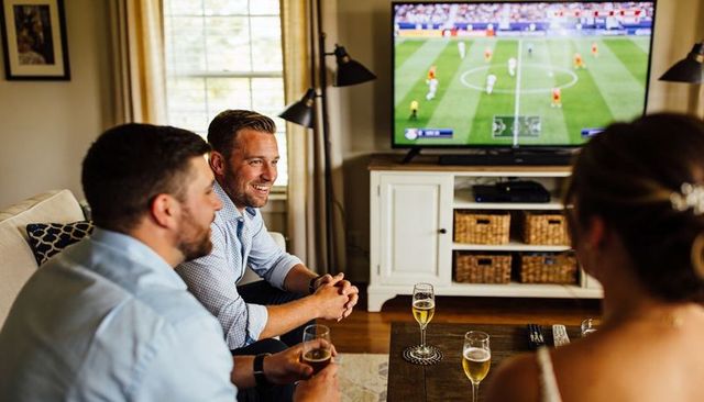 Friends watching soccer at home, men laughing and enjoying game night in cozy living room