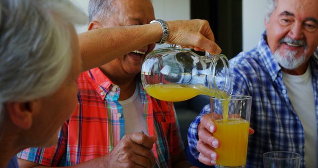 Happy seniors gather and enjoy pouring fresh orange juice into glasses. Perfect for depicting friendship, joyful moments, and a relaxed atmosphere. Can be used for senior living advertisements, healthy lifestyle promotions, and social event marketing.