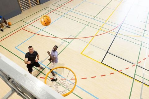 Jumping male players reaching for rebound at indoor basketball hoop during practice