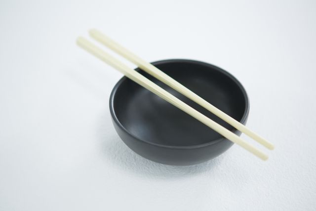 Close-up view of a black bowl with chopsticks placed across it on a white background. Perfect for use in articles or advertisements related to Asian cuisine, minimalist dining, modern kitchenware, or tableware products. Great for illustrating simplicity and elegance in food presentation.