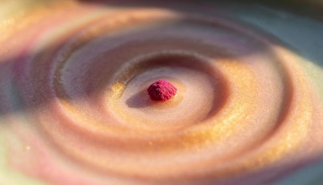 Magenta powder mound on pearlescent spiral surface macro still life with gold iridescence