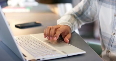 Man using laptop touchpad in plaid shirt with smartphone for remote work productivity