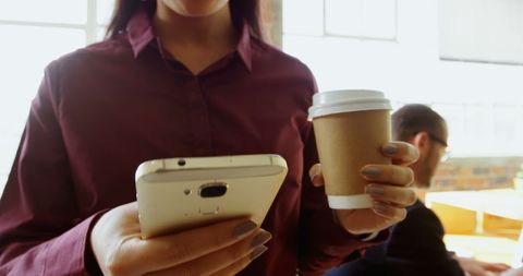 Businesswoman Checking Smartphone While Holding Coffee Cup in Office - Download Free Stock Images Pikwizard.com