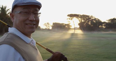 Happy golfer holding club with sunlit golf course background