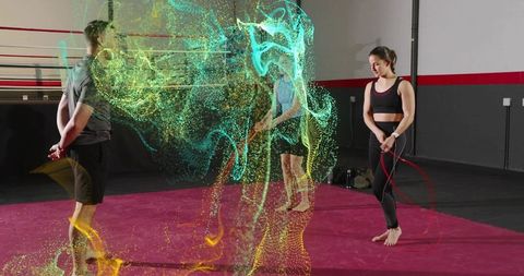Workout partners holding jump ropes barefoot on boxing mat with neon particle trails