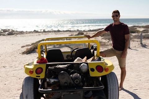 Man enjoying ocean view with yellow dune buggy on sunny beach