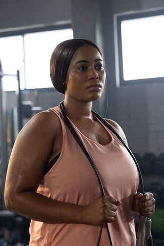 African american woman training with jump rope in gym, sweating, focused, wearing dusty pink tank