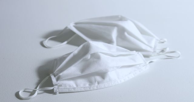 Close-up of two white cloth face masks on a white background. Ideal for use in articles and websites focusing on health, safety, personal protection, and hygiene. Can be used in materials related to the COVID-19 pandemic, medical equipment, or home-made protective gear.